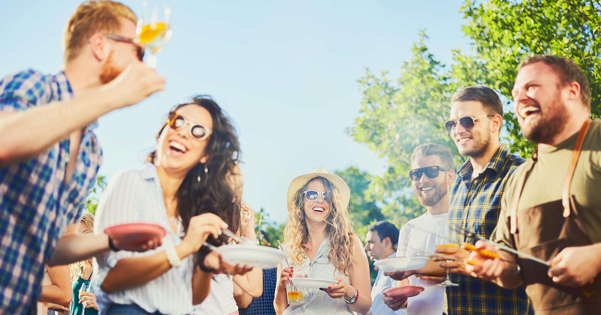 People gathered together drinking alcohol and eating food outside while smiling.